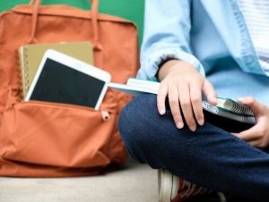 Student's hand in lap with notebooks and bookbag