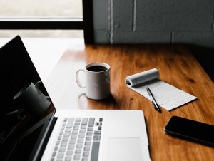 Laptop, coffee cup and notepad on top of a desk