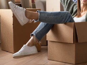Woman sitting in cardboard moving box, kicking feet out