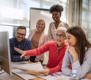 A group of racially and age diverse people sitting at a computer smiling