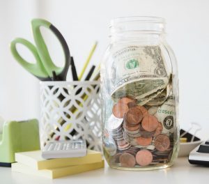 A jar of money and change on a desk.