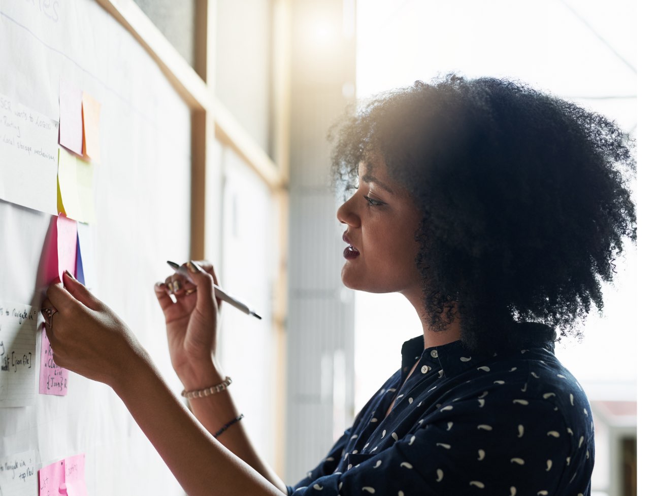 African American woman looking at post it notes on a board