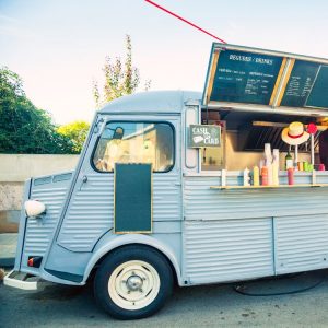 A light blue food truck on a street with the service window open