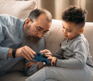 Grandfather playing with young grandson on couch.