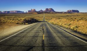 Open road running through desert with blue sky and mountains in the background
