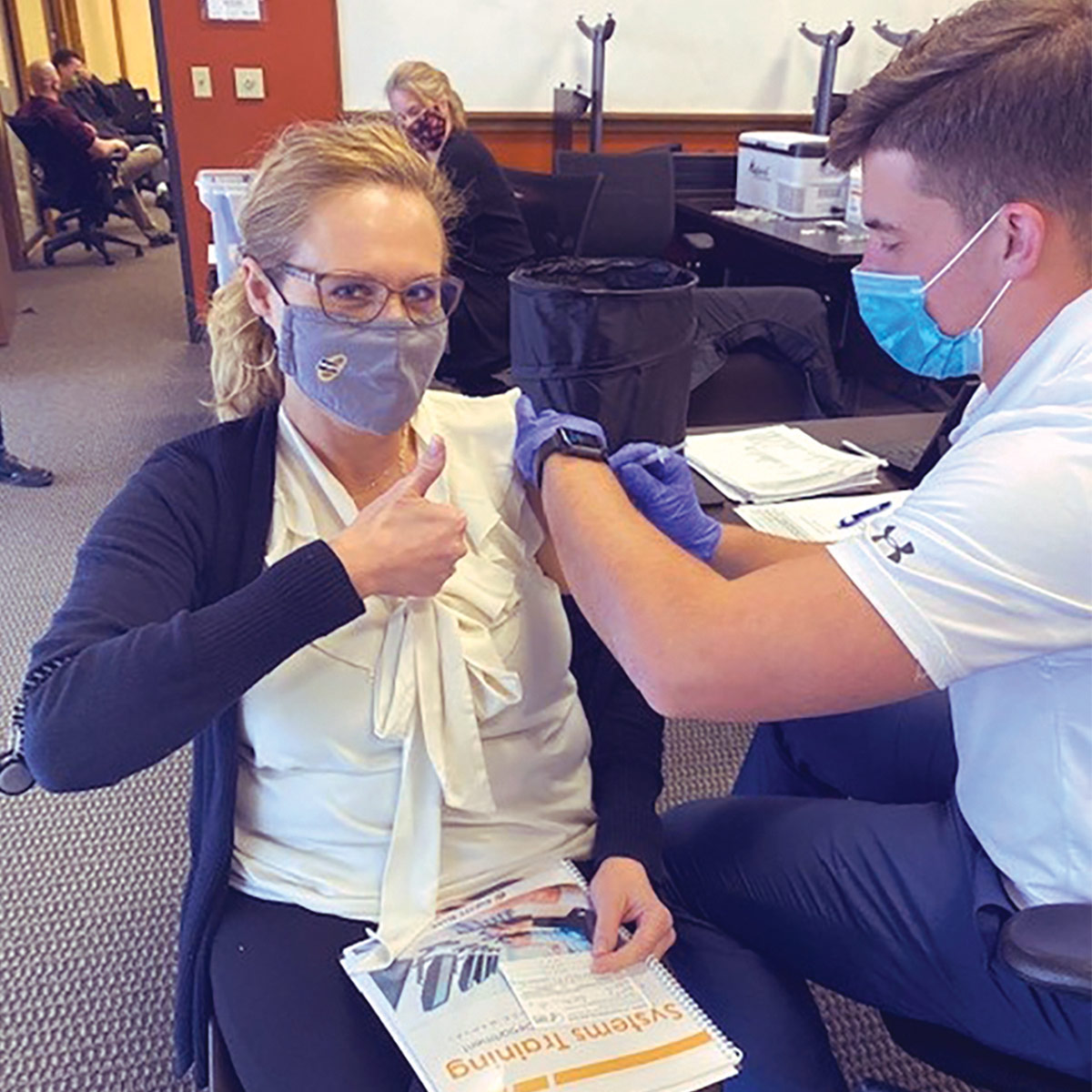 Woman gives thumbs-up as she gets a vaccination shot.