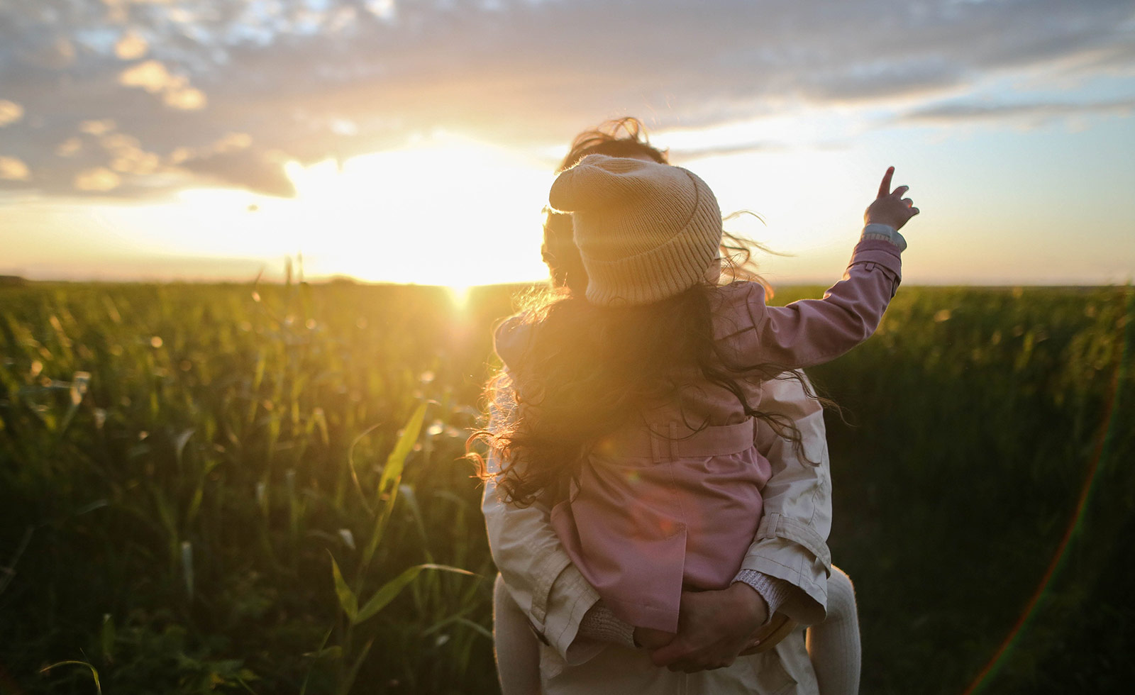 Parent and child in a field with dramatic skyline.