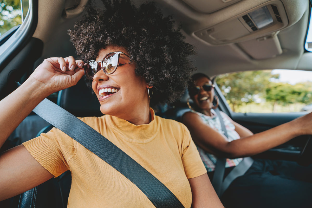 A happy woman in the passenger seat of a car looking out the window.