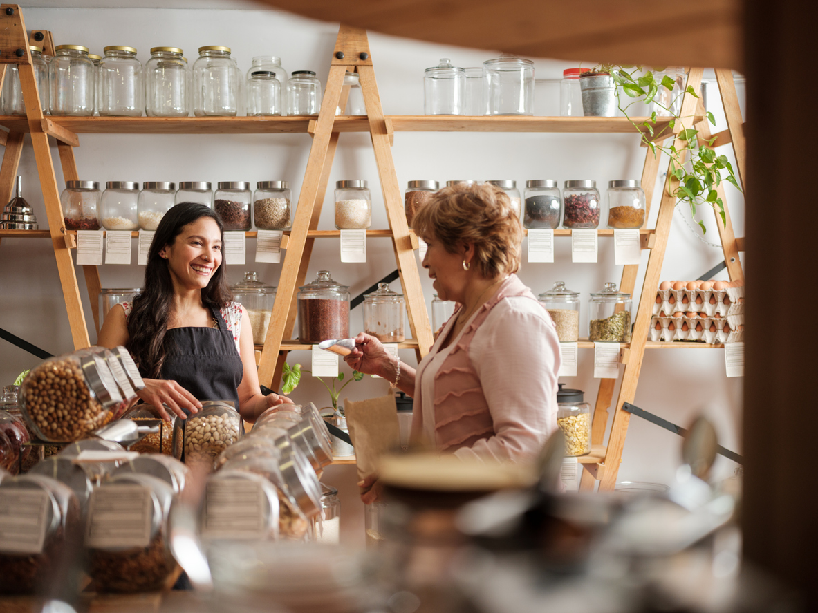 Small business owner assisting a customer in a local retail shop with jars of bulk goods on shelves