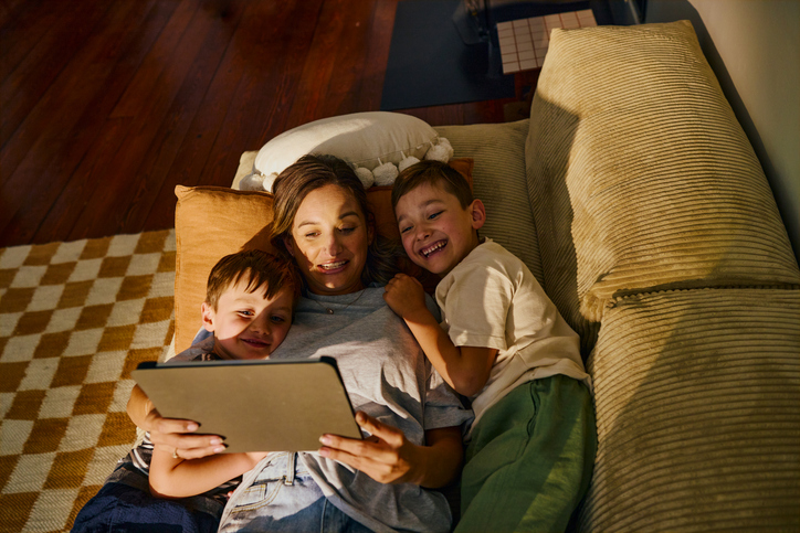 Mother and two kids cuddled on a sofa, looking at a tablet together.