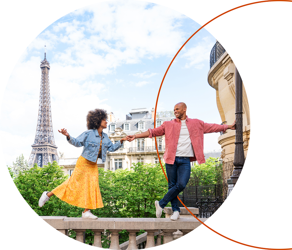 Couple dancing hand-in-hand on a Paris balcony with the Eiffel Tower in the background on a sunny day.