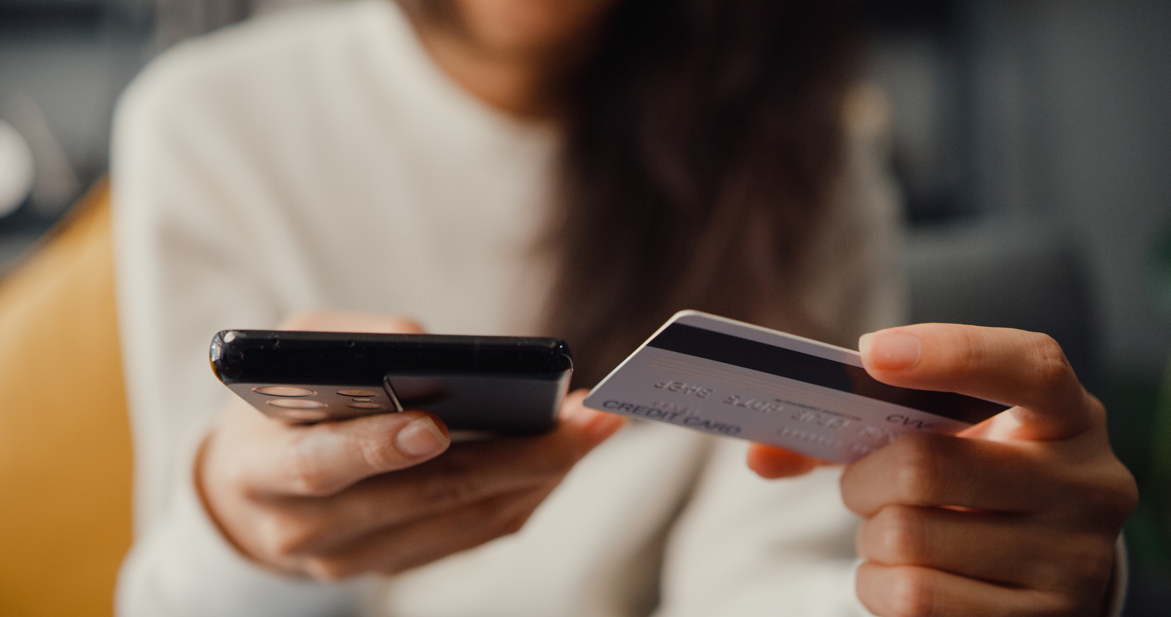 Person holds a smartphone in one hand and a credit card in the other, as if making a payment online.