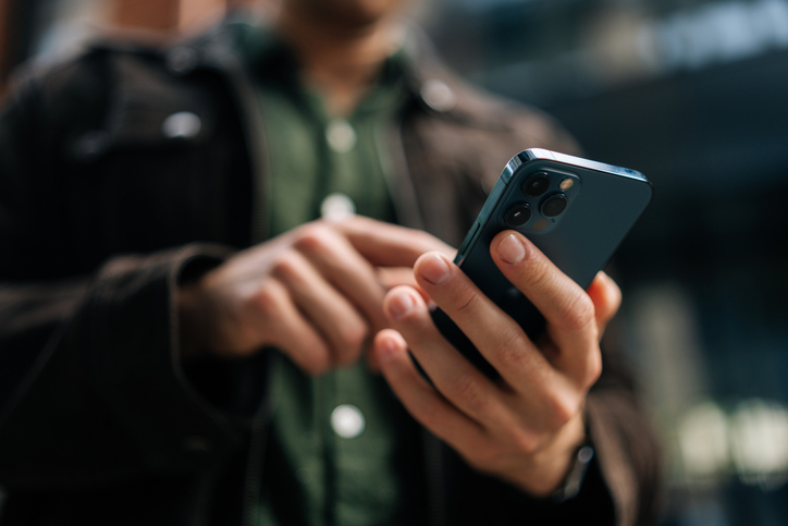 Person outdoors, holding and using a blue smartphone with both hands