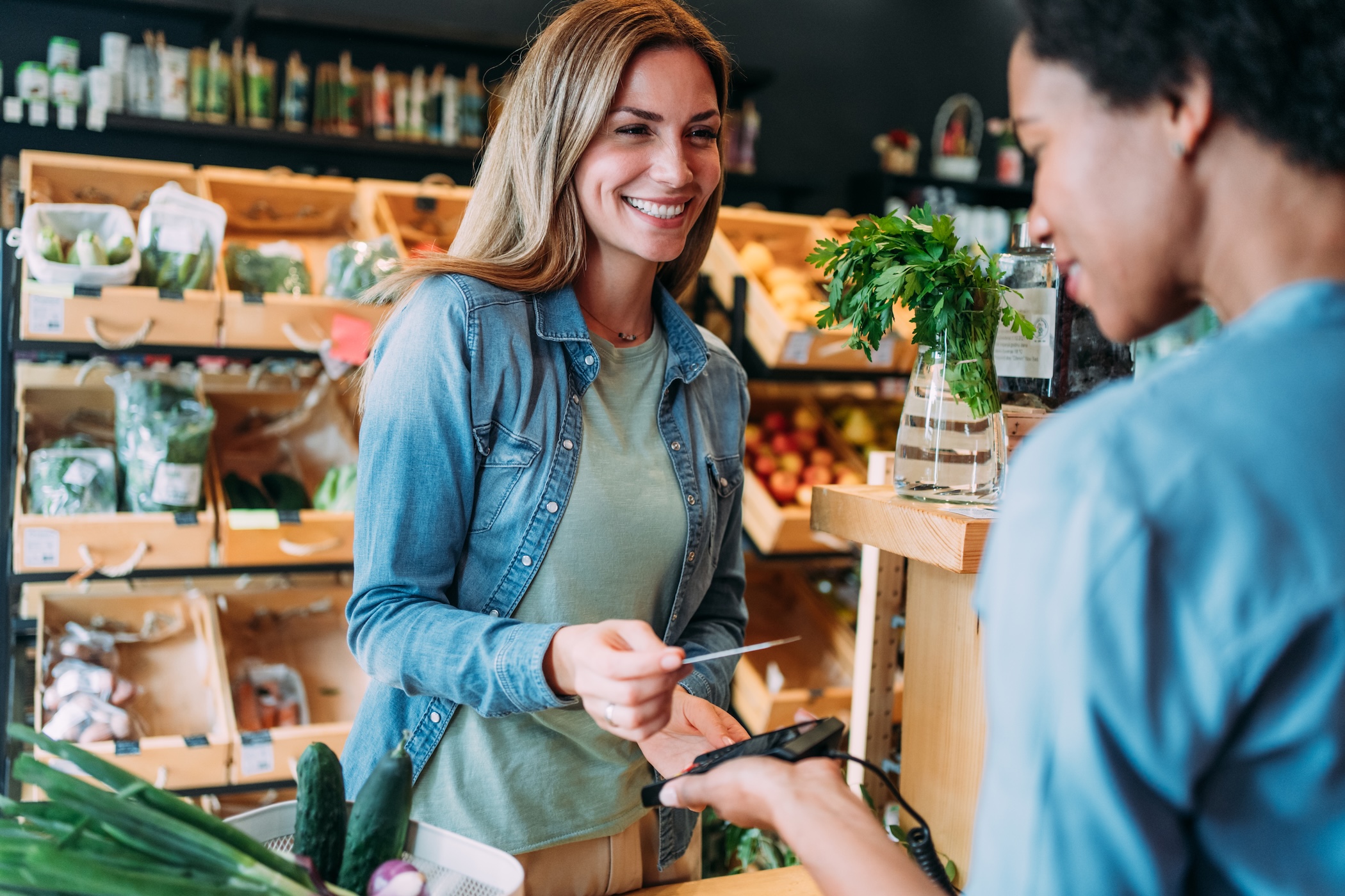 Smiling woman paying with a card at a local grocery market checkout, illustrating everyday spending and buying power