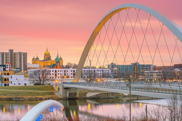 Sunset over a city with a large white arch bridge crossing a calm river; illuminated domed building and modern buildings in the background.